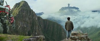 Movie still from “Transformers: Rise of the Beasts” (2023), directed by Steven Caple Jr. – A man standing on top of a mountain looking at the sky; Extreme Wide shot, Low angle