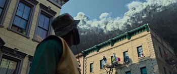 Movie still from “Transformers: Rise of the Beasts” (2023), directed by Steven Caple Jr. – A man standing on a fire escape looking at smoke billowing from a building; Extreme Wide shot, Low angle