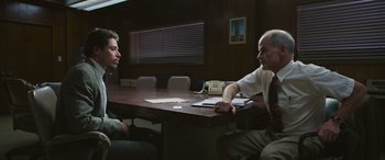 Movie still from “Transformers: Rise of the Beasts” (2023), directed by Steven Caple Jr. – Two men sitting at a table in front of papers; Medium shot, Over the shoulder angle