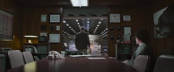 Movie still from “Transformers: Rise of the Beasts” (2023), directed by Steven Caple Jr. – A man in a suit standing in front of a table; Wide shot, Low angle