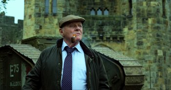 Movie still from “Transformers: The Last Knight” (2017), directed by Michael Bay – An older man smoking a pipe in front of an old building; Medium shot, Low angle