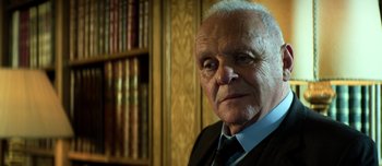 Movie still from “Transformers: The Last Knight” (2017), directed by Michael Bay – An older man wearing a suit and tie in front of a book case; Close Up shot, Low angle