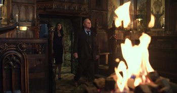 Movie still from “Transformers: The Last Knight” (2017), directed by Michael Bay – A man and a woman walking in front of a fireplace; Wide shot, Over the shoulder angle