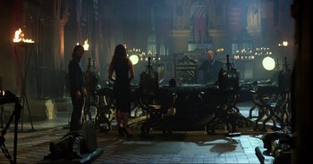 Movie still from “Transformers: The Last Knight” (2017), directed by Michael Bay – A group of people standing around a long table; Wide shot, Over the shoulder angle