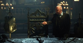 Movie still from “Transformers: The Last Knight” (2017), directed by Michael Bay – An old man in a black suit is holding a sword; Wide shot, Over the shoulder angle