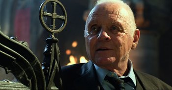 Movie still from “Transformers: The Last Knight” (2017), directed by Michael Bay – An older man in a suit and tie holding a crucifixion; Close Up shot, Low angle