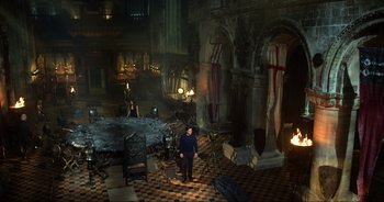 Movie still from “Transformers: The Last Knight” (2017), directed by Michael Bay – A man standing in front of a table in a room; Extreme Wide shot, High angle