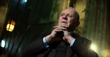 Movie still from “Transformers: The Last Knight” (2017), directed by Michael Bay – An older man wearing a suit and tie holding his hands to his chin; Close Up shot, Low angle