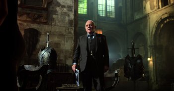 Movie still from “Transformers: The Last Knight” (2017), directed by Michael Bay – An older man in a suit stands in a dark room; Medium shot, Low angle