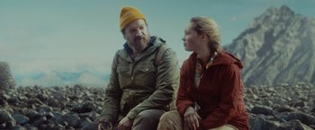 Movie still from “Troll” (2022), directed by Roar Uthaug – A man and a woman sitting next to each other on rocks; Medium shot, Low angle