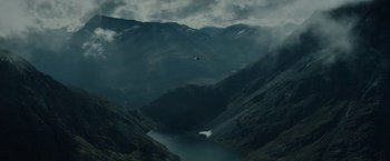 Movie still from “Troll” (2022), directed by Roar Uthaug – A helicopter flying over a lake in the middle of a valley; Extreme Wide shot, High angle