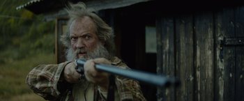 Movie still from “Troll” (2022), directed by Roar Uthaug – An old man with a beard holding a gun; Close Up shot, Low angle