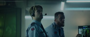 Movie still from “Troll” (2022), directed by Roar Uthaug – Two men in uniforms are wearing headphones and looking up; Close Up shot, Low angle