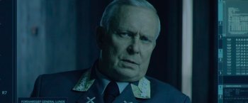 Movie still from “Troll” (2022), directed by Roar Uthaug – An older man wearing a uniform with crosses on it; Close Up shot, Over the shoulder angle