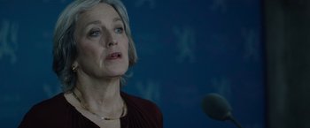 Movie still from “Troll” (2022), directed by Roar Uthaug – An older woman is speaking in front of a microphone; Close Up shot, Over the shoulder angle