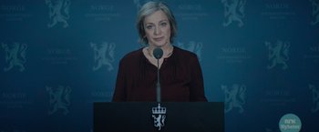 Movie still from “Troll” (2022), directed by Roar Uthaug – A woman standing at a podium in front of microphones; Close Up shot, Low angle