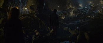 Movie still from “Troll” (2022), directed by Roar Uthaug – A man standing in a cave filled with lots of skulls; Extreme Wide shot, High angle