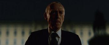 Movie still from “Troll” (2022), directed by Roar Uthaug – An older man in a suit and tie; Close Up shot, Low angle