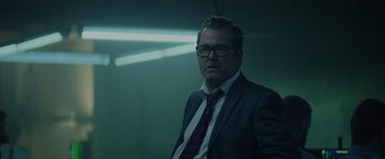 Movie still from “Troll” (2022), directed by Roar Uthaug – A man in a suit and tie standing in a dark room; Medium shot, Low angle