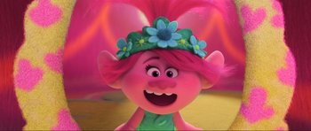 Movie still from “Trolls World Tour” (2020), directed by Walt Dohrn – A pink haired troll with a flower crown on her head; Close Up shot, Low angle