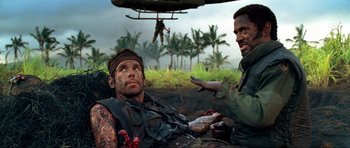 Movie still from “Tropic Thunder” (2008), directed by Ben Stiller – Two men are sitting in a field with a helicopter in the background; Medium shot, Over the shoulder angle