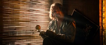 Movie still from “Tropic Thunder” (2008), directed by Ben Stiller – A man sitting in front of a window holding an apple; Close Up shot, Low angle