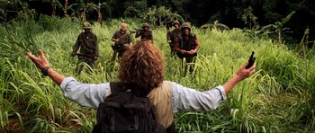 Movie still from “Tropic Thunder” (2008), directed by Ben Stiller – A group of people in the grass with a backpack; Wide shot, Over the shoulder angle