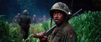 Movie still from “Tropic Thunder” (2008), directed by Ben Stiller – A man holding a rifle and wearing an army helmet; Close Up shot, Over the shoulder angle