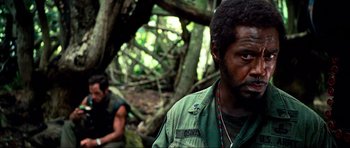 Movie still from “Tropic Thunder” (2008), directed by Ben Stiller – A man in a green shirt is standing in the woods; Close Up shot, Over the shoulder angle