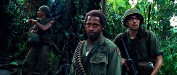 Movie still from “Tropic Thunder” (2008), directed by Ben Stiller – A man in a military uniform standing next to a tree; Medium shot, Over the shoulder angle