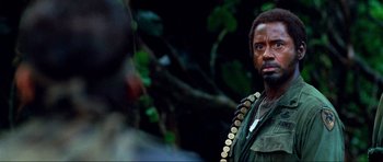Movie still from “Tropic Thunder” (2008), directed by Ben Stiller – A man in a military uniform standing in front of a tree; Close Up shot, Over the shoulder angle