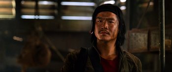 Movie still from “Tropic Thunder” (2008), directed by Ben Stiller – A man with long black hair wearing a red shirt; Close Up shot, Low angle