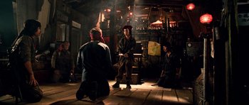 Movie still from “Tropic Thunder” (2008), directed by Ben Stiller – A group of people sitting on the ground in a room; Wide shot, Over the shoulder angle