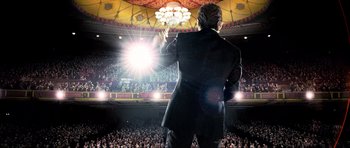 Movie still from “Tropic Thunder” (2008), directed by Ben Stiller – A man in a black suit is on a stage with a crowd; Wide shot, Low angle