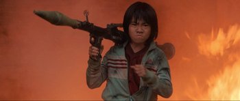 Movie still from “Tropic Thunder” (2008), directed by Ben Stiller – A young boy holding a gun in his hands; Medium shot, Low angle