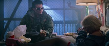 Movie still from “True Romance” (1993), directed by Tony Scott – A man sitting on a couch eating a hot dog; Medium shot, Low angle