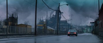 Movie still from “True Romance” (1993), directed by Tony Scott – A car driving down a street near a factory; Extreme Wide shot, Low angle