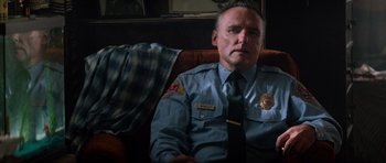 Movie still from “True Romance” (1993), directed by Tony Scott – A police officer sitting on a couch in a living room; Medium shot, Low angle