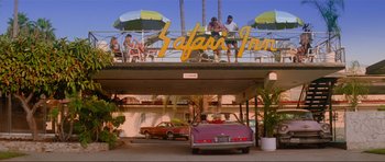 Movie still from “True Romance” (1993), directed by Tony Scott – A car parked in front of a hotel with a lot of people sitting on top of it; Wide shot, Low angle