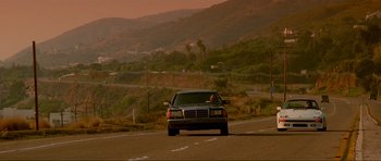 Movie still from “True Romance” (1993), directed by Tony Scott – A car driving down a road near a mountain range; Extreme Wide shot, Over the shoulder angle
