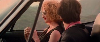 Movie still from “True Romance” (1993), directed by Tony Scott – A woman with red curly hair sitting in the passenger seat of a car; Medium shot, Over the shoulder angle