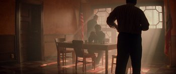 Movie still from “True Romance” (1993), directed by Tony Scott – Two men sitting at a table in front of an american flag; Wide shot, Low angle