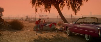 Movie still from “True Romance” (1993), directed by Tony Scott – Two people sitting on a couch under a tree; Wide shot, High angle