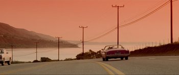Movie still from “True Romance” (1993), directed by Tony Scott – A car driving down a road next to a body of water; Extreme Wide shot, High angle