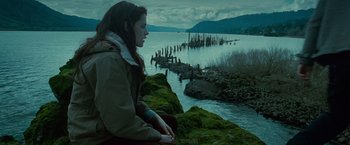 Movie still from “Twilight” (2008), directed by Catherine Hardwicke – A woman sitting on top of a rock next to a body of water; Wide shot, High angle