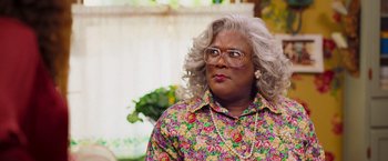 Movie still from “Tyler Perry's A Madea Homecoming” (2022), directed by Tyler Perry – A woman in a floral shirt and glasses looks to her left; Close Up shot, High angle