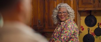 Movie still from “Tyler Perry's A Madea Homecoming” (2022), directed by Tyler Perry – A woman in a floral shirt standing next to a wooden cabinet; Close Up shot, Over the shoulder angle