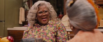 Movie still from “Tyler Perry's A Madea Homecoming” (2022), directed by Tyler Perry – A woman in a floral shirt is sitting at a table; Close Up shot, Over the shoulder angle