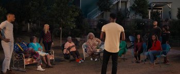 Movie still from “Tyler Perry's A Madea Homecoming” (2022), directed by Tyler Perry – A group of people sitting in a yard at night; Extreme Wide shot, Over the shoulder angle