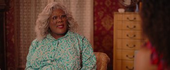 Movie still from “Tyler Perry's A Madea Homecoming” (2022), directed by Tyler Perry – A madea character sitting in a chair in front of a dresser; Close Up shot, Over the shoulder angle